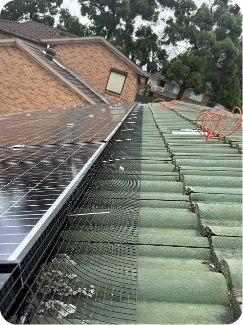 Bird proofing mesh being installed along the edge of rooftop solar panels using panel mounting clips