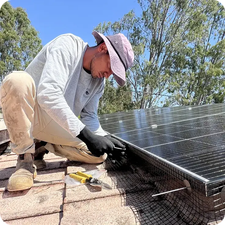 Technician securing bird proofing mesh to the edge of rooftop solar panels using solar panel clips